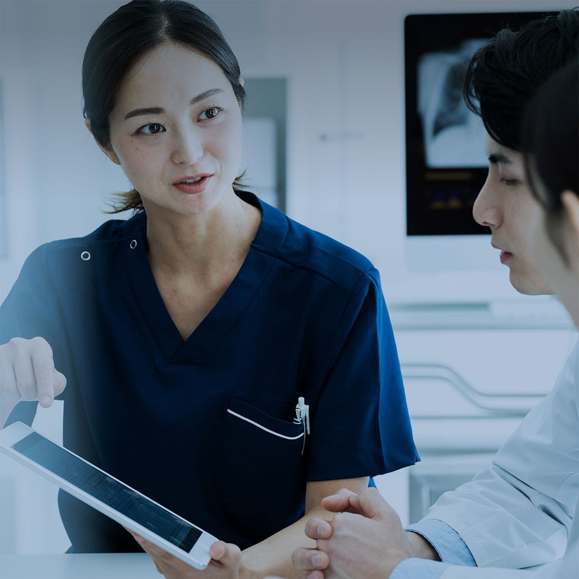 医療従事者の女性が、同僚たちと真剣に話し合いをしている場面。地域医療の連携やチーム医療を象徴