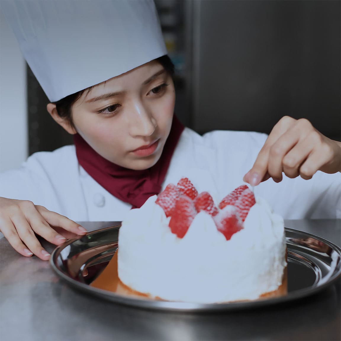 パティシエの女性が、ケーキに丁寧にデコレーションを施している場面。地域文化や食のつながりを象徴